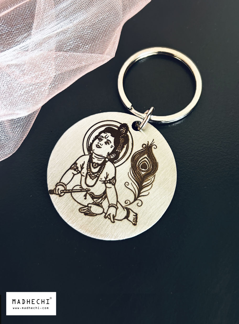 A stainless steel keychain with an engraving of Baby Kanha,